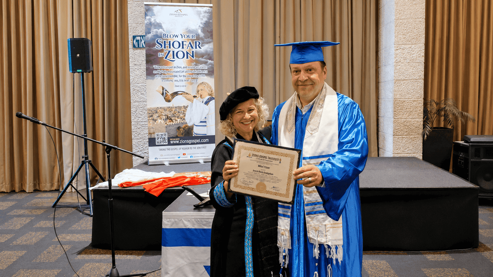 Graduate in blue cap and gown receiving diploma at graduation ceremony.